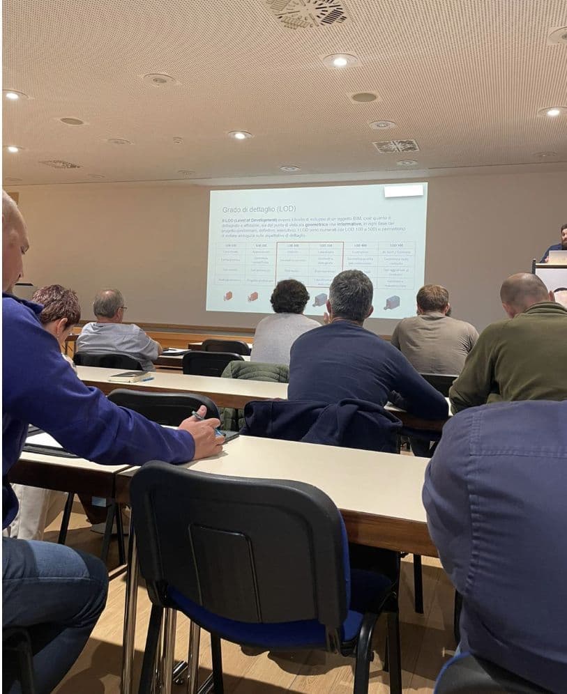 Besprechung in einem Konferenzraum: Mehrere Personen sitzen an Tischen und schauen auf eine Präsentation an der Leinwand.