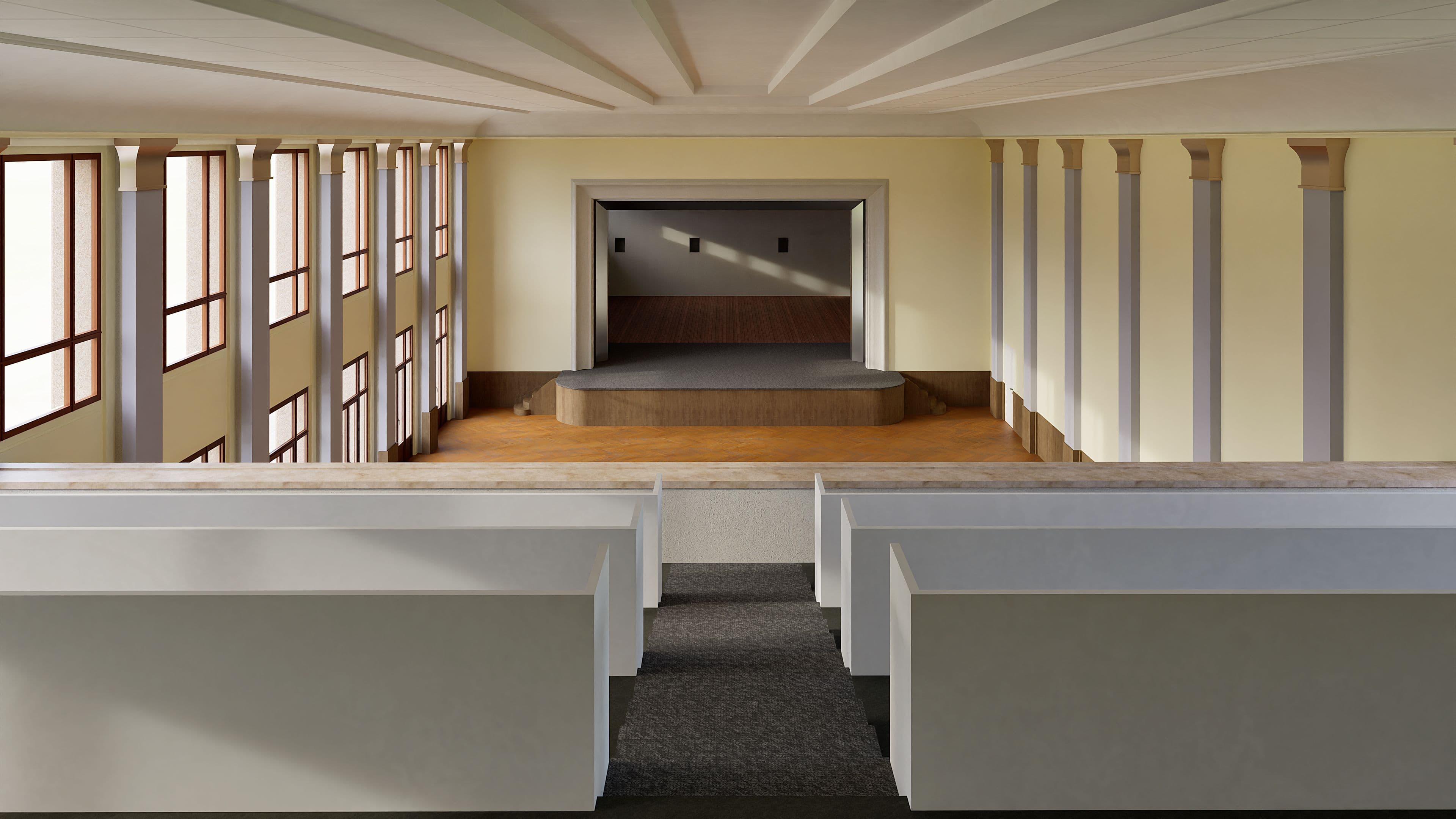 Großer Raum mit Sitzreihen und Bühne, beleuchtet durch große Fenster auf der linken Seite.