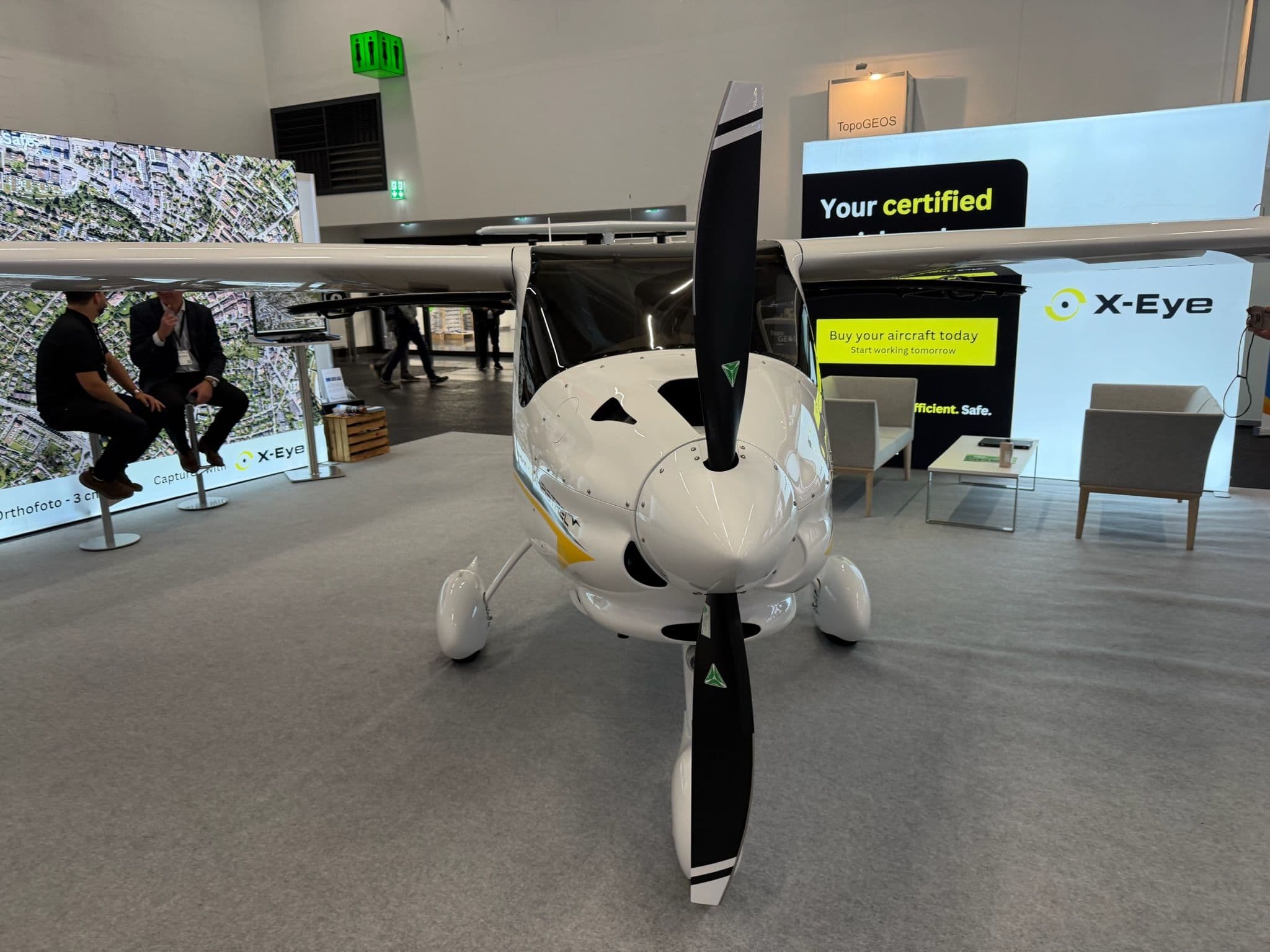 Kleines Flugzeug auf Messe, vorne mit Propeller. Hintergrund: X-Eye-Stand, Personen in Gespräch.