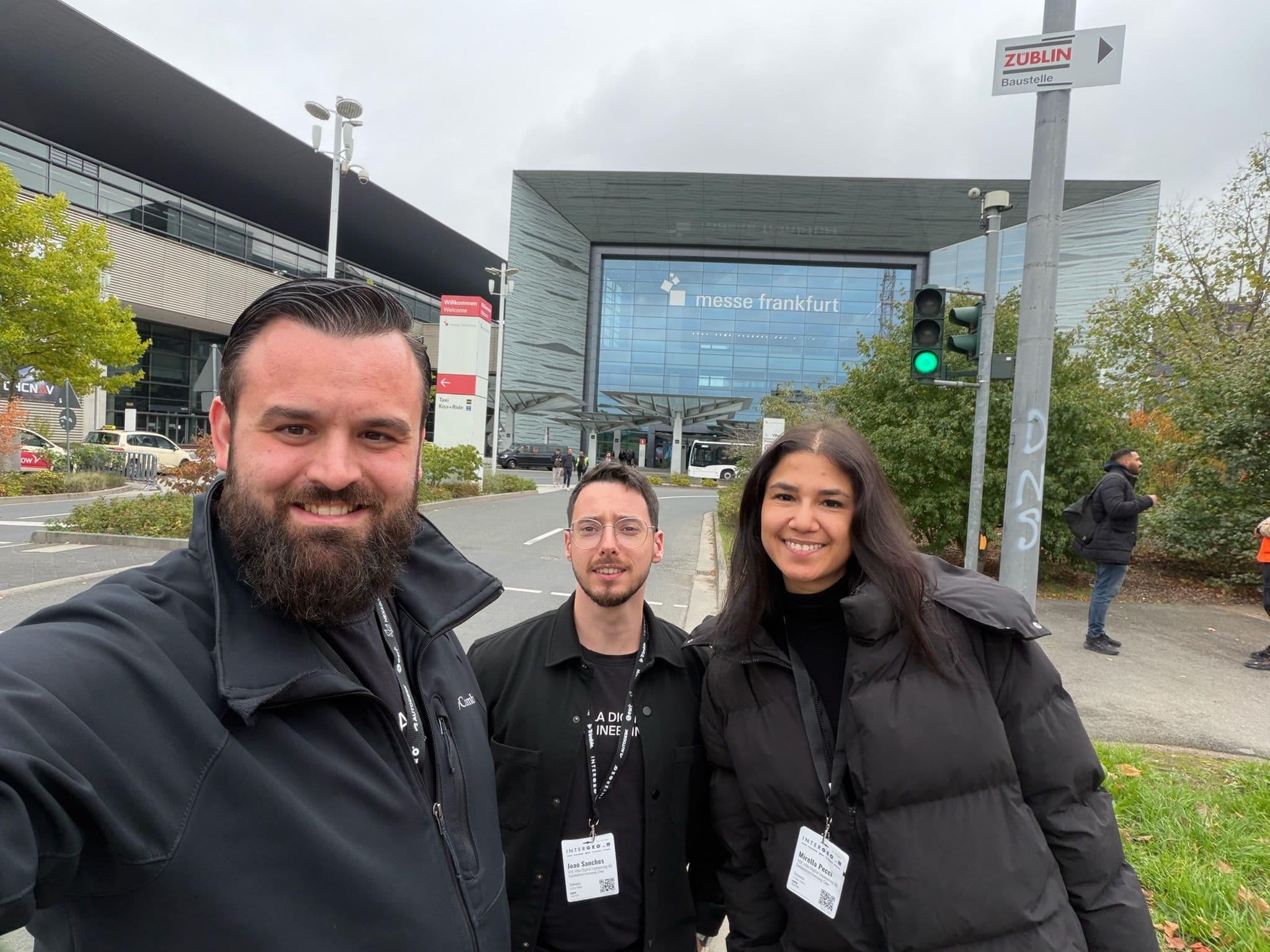 Messe Frankfurt Eingang mit drei Personen im Vordergrund, die Namensschilder tragen.