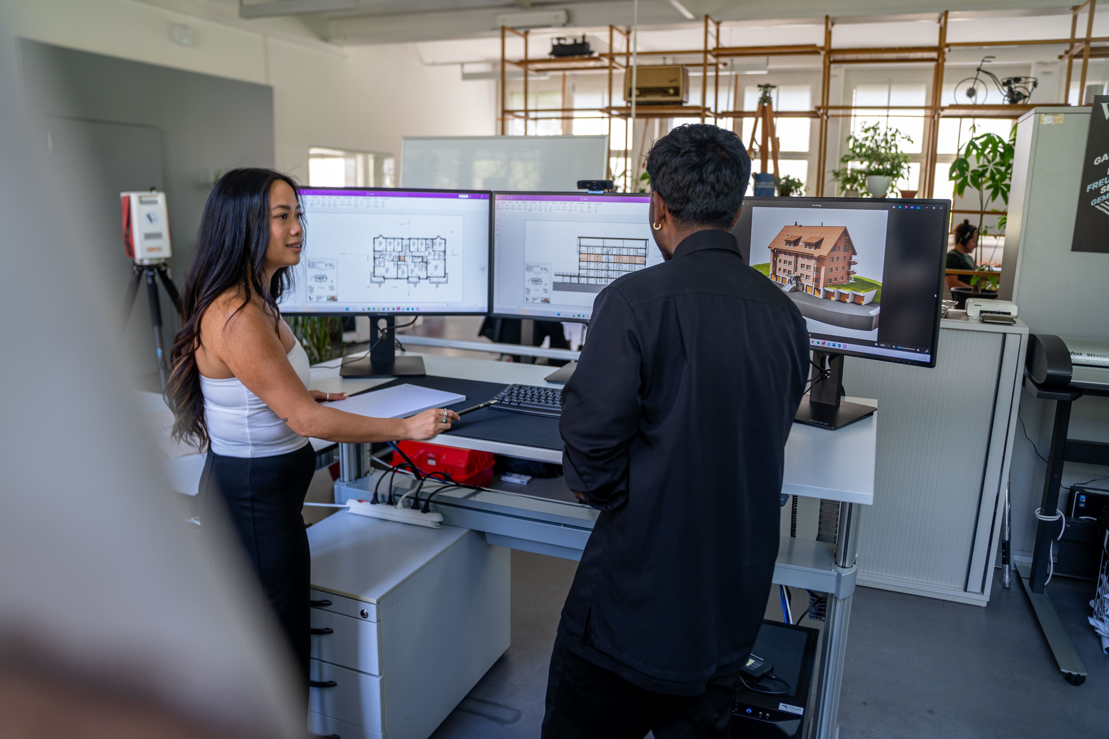 Zwei Personen arbeiten in einem modernen Büro an Computern mit Architektur-Software.