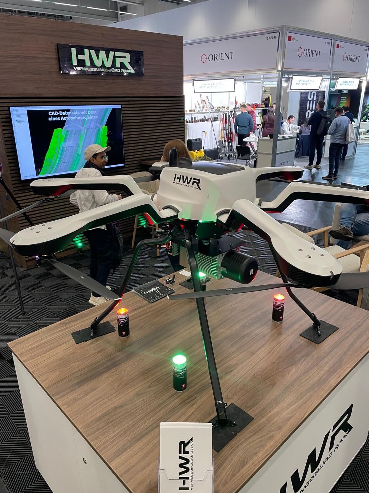 Drohnen-Display von HWR auf einer Messe, mit großem Quadrocopter auf Tisch und grün-rotem Lichtsignal, umgeben von Besuchern.