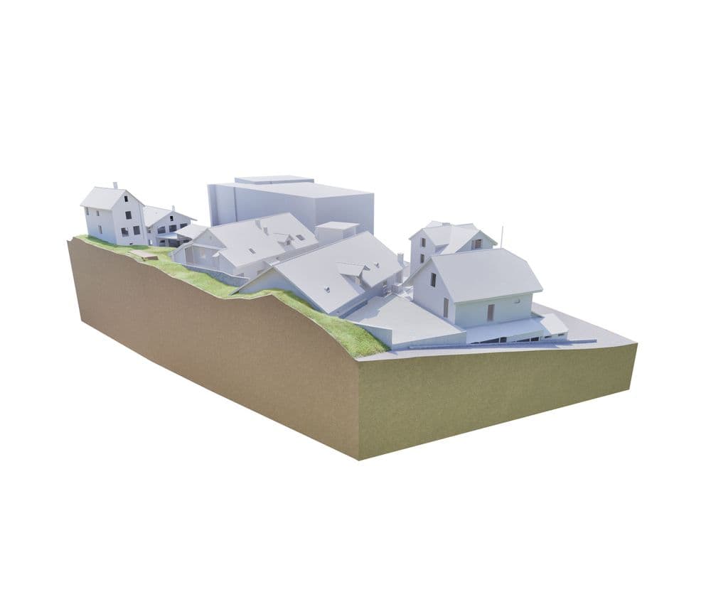 3D-Modell einer hügeligen Landschaft mit mehreren weißen Gebäuden auf unterschiedlichen Ebenen, grüne Bereiche markieren Vegetation.