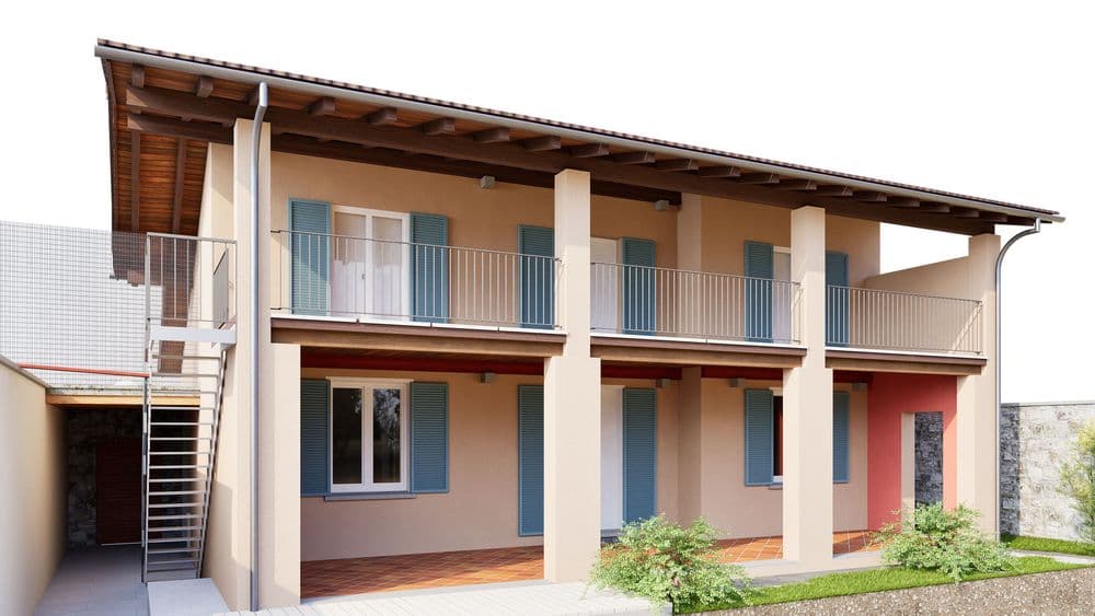 Zweistöckiges Haus mit blauen Fensterläden und Balkon, daneben eine Außentreppe, umgeben von Rasen.