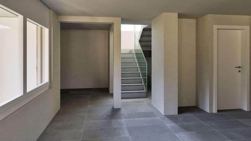Modernes Treppenhaus in einem Gebäude mit grauen Fliesen und großen Fenstern.