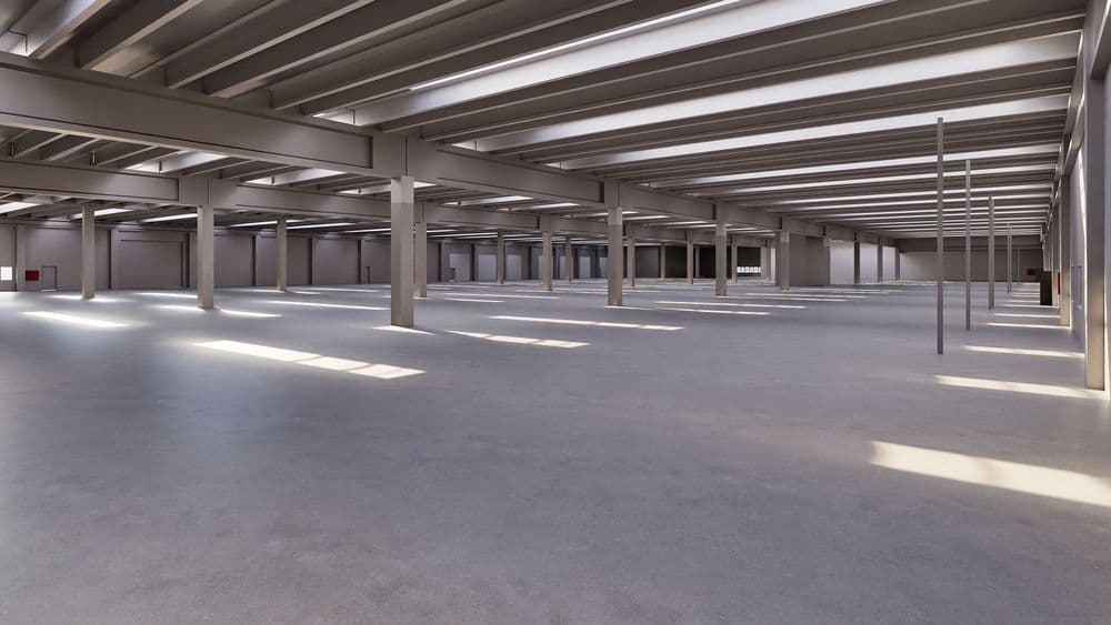 Weiträumige, leere industrielle Lagerhalle mit sichtbaren Stahlträgern und natürlichem Lichteinfall.