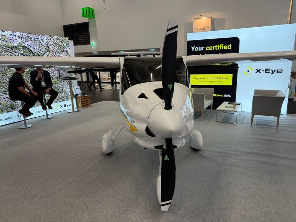 Kleines Flugzeug auf Messe, vorne mit Propeller. Hintergrund: X-Eye-Stand, Personen in Gespräch.