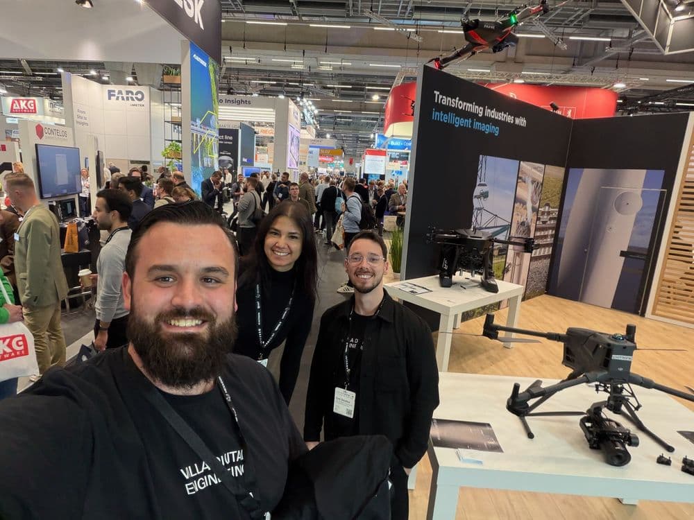 Gruppenfoto auf einer Messe mit Technologie- und Drohnenpräsentation im Hintergrund.