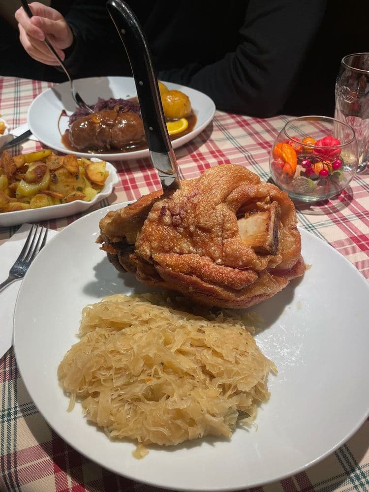 Knusprige Schweinshaxe mit Sauerkraut und Bratkartoffeln auf kariertem Tischtuch.