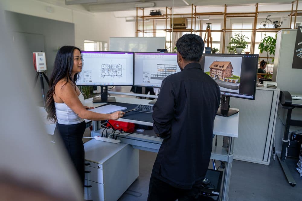 Zwei Personen arbeiten in einem modernen Büro an Computern mit Architektur-Software.