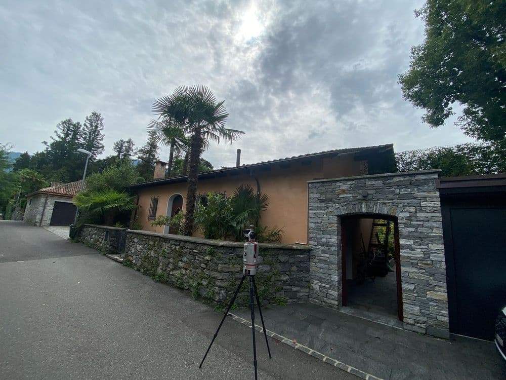 Straßenansicht eines Hauses mit Steinmauer und Palme, bewölkter Himmel.