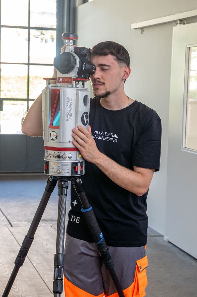 Ein Mann verwendet ein Vermessungsgerät in einem Raum mit großen Fenstern.