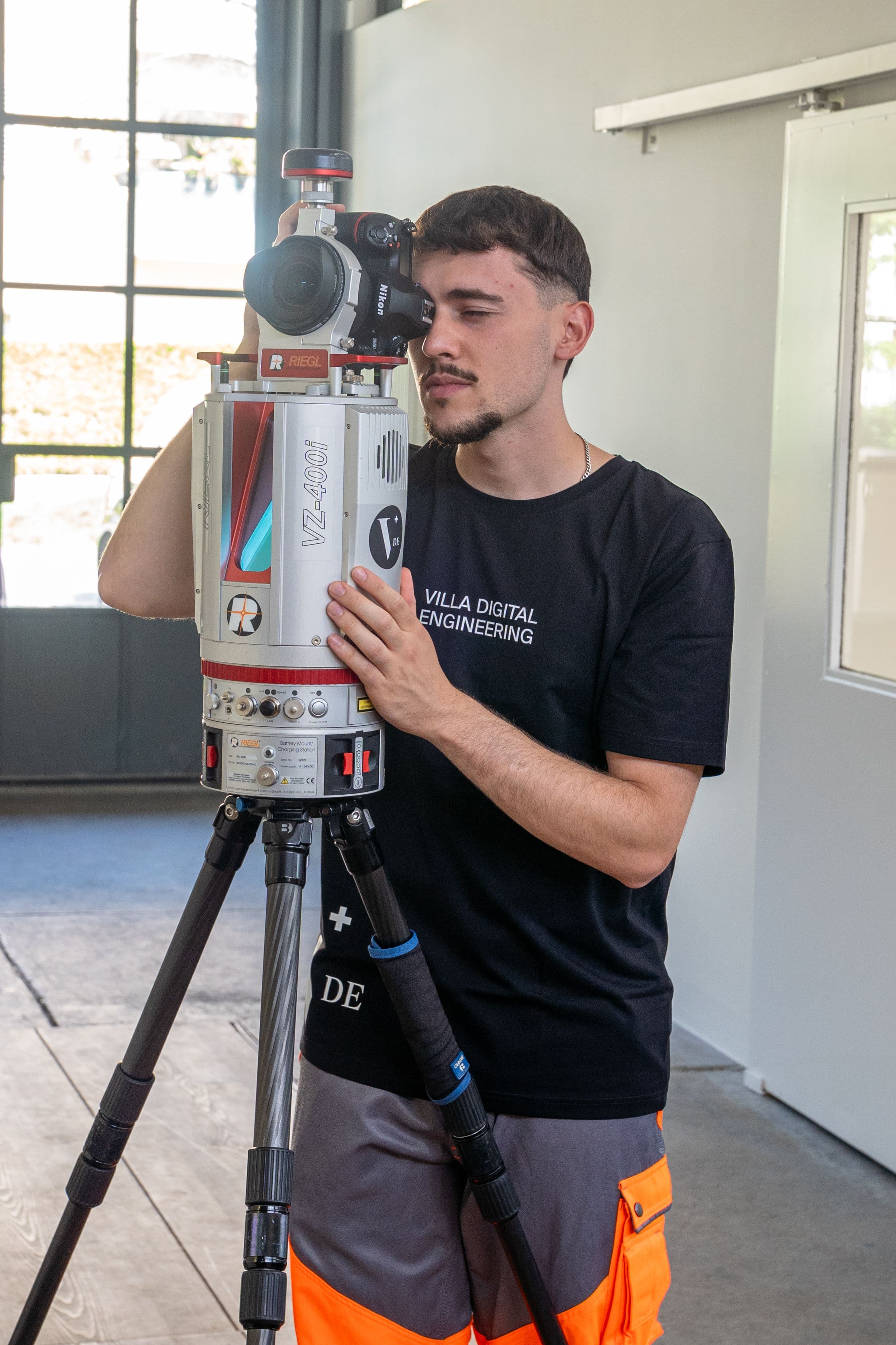 Ein Mann verwendet ein Vermessungsgerät in einem Raum mit großen Fenstern.